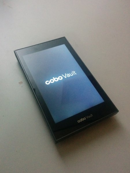 A Cobo Vault cryptocurrency hardware wallet is displayed on a flat surface. The screen shows the device logo and name, much like the sleek design of the Keystone 3 Pro.