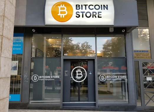 Front view of a storefront labeled "Bitcoin Store," featuring a large Bitcoin symbol above the entrance, and two Bitcoin logos on the glass windows beside the door, offering customers the option to acquire Bitcoin without ID verification.