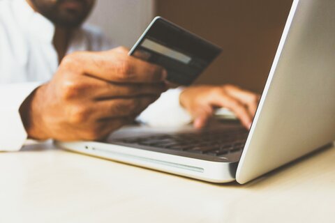 A person holding a credit card in one hand and typing on a laptop with the other, exploring how to acquire Bitcoin without ID verification.