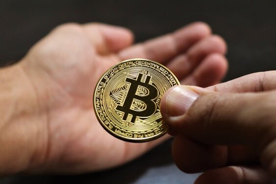 A close-up shot of a person holding a physical Bitcoin coin in their right hand, with an open left hand visible under it, symbolizes the ease with which one can acquire Bitcoin without ID verification.