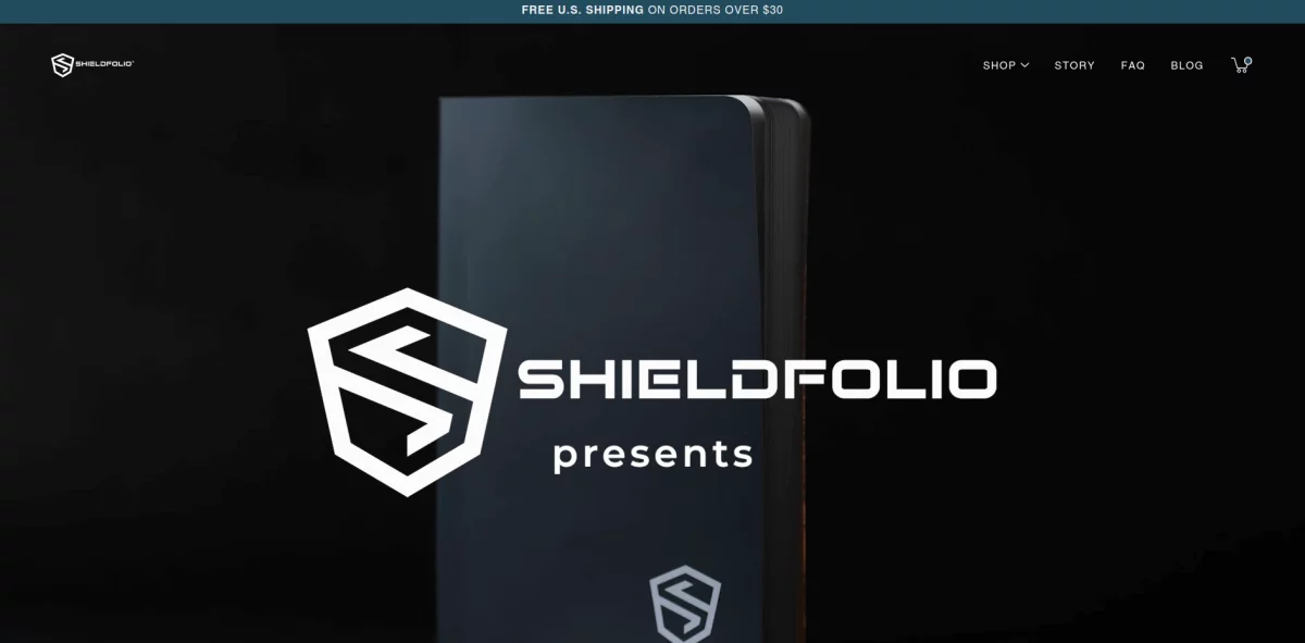 Front page of the Shieldfolio website displaying a product and logo, with text indicating 15% Off Your Next Purchase at Shieldfolio! Enjoy free U.S. shipping on orders over $50.